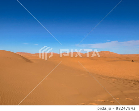 The sahara desert and its sand dunes with a blue sky as a background. The sahara desert and its sand dunes with a blue sky as a background. 98247943