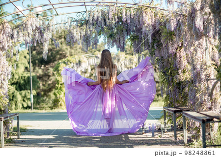 Thoughtful happy mature woman surrounded by chinese wisteria in purple dress Thoughtful happy mature woman surrounded by chinese wisteria in purple dress 98248861