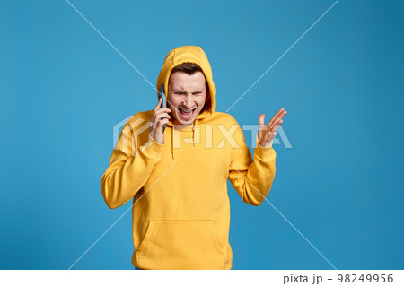 angry man in yellow sweatshirt holding mobile phone 98249956