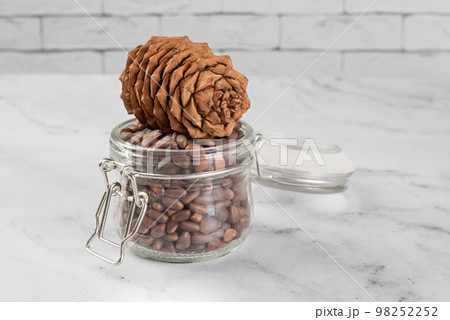 Pine nuts in a jar and a pine cone in the kitchen on a light background. Pine nuts in a jar and a pine cone in the kitchen on a light background. 98252252