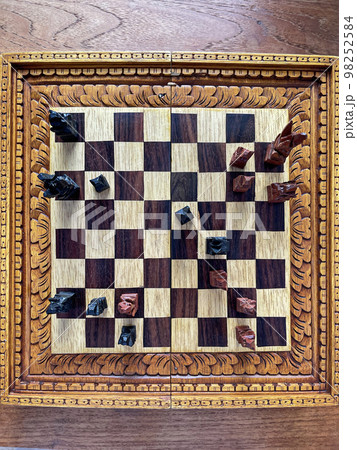 Top view of a chessboard with handmade carved pieces. Black and white shapes. Intelligent game. Competitive spirit. Top view of a chessboard with handmade carved pieces. Black and white shapes. Intelligent game. Competitive spirit. 98252584