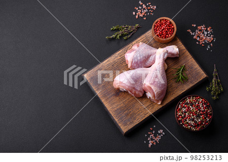 Three raw chicken legs with spices and herbs on a wooden cutting board 98253213