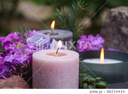 Closeup burning candles purple flowers stone on blurred background Closeup burning candles purple flowers stone on blurred background 98254434
