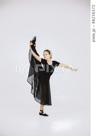 Little ballerina on white background. Brunette girl wearing black ballet suit. Girl doing gymnastic excercises. 98256372