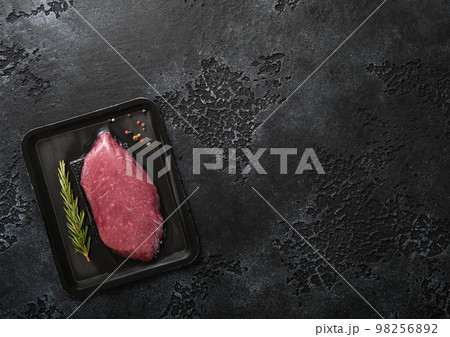 Fresh raw beef fillet steak sealed in vacuum tray with pepper and rosemary on black 98256892