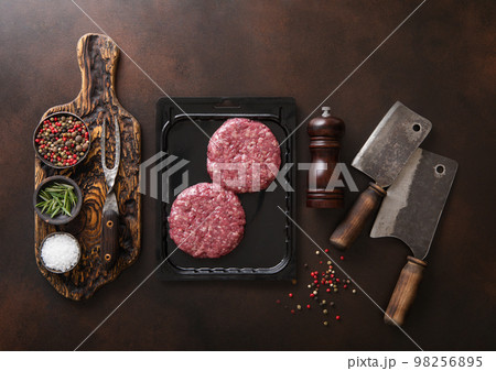 Raw beef burgers sealed in vacuum tray with cleavers on dark kitchen table with pepper grinde Raw beef burgers sealed in vacuum tray with cleavers on dark kitchen table with pepper grinde 98256895