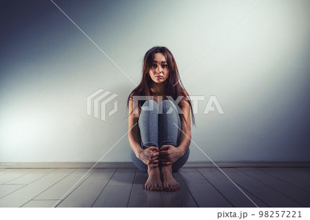 A young sad woman sits disheveled on the floor of a room. There is a light wall in the background.Human trafficking, sexual slavery concept. Copy space 98257221