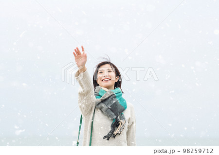 雪が降る空に向かって手を伸ばす女性 98259712