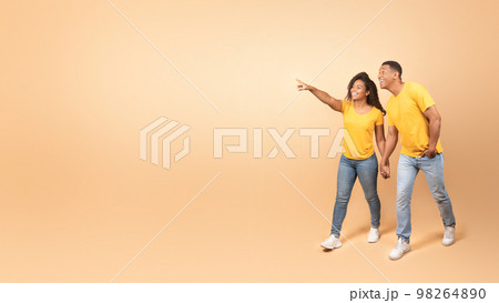 Happy african american couple walking and holding hands, woman pointing finger to free space, panorama 98264890