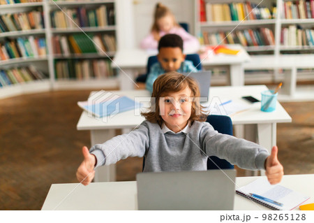 Education concept. Group of diverse classmates sitting at desk in classroom, caucasian boy showing thumbs up Education concept. Group of diverse classmates sitting at desk in classroom, caucasian boy showing thumbs up 98265128