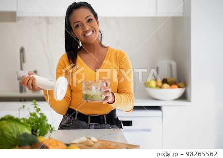 Happy young african american woman making smoothie with blender at table with organic vegetables 98265562