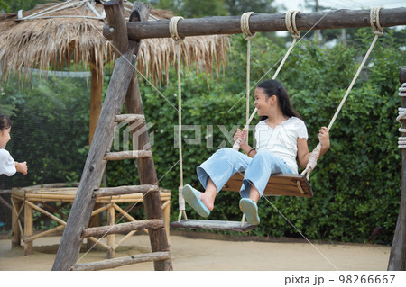 Happy girl playing on the wooden swing in the playground. Happy girl playing on the wooden swing in the playground. 98266667