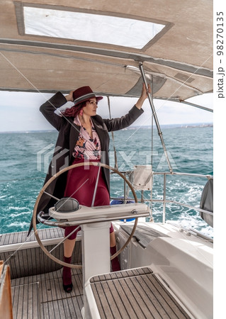 Attractive middle-aged woman at the helm of a yacht on a summer day. Luxury summer adventure, outdoor activities. Attractive middle-aged woman at the helm of a yacht on a summer day. Luxury summer adventure, outdoor activities. 98270135