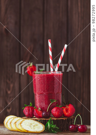 Side view of glass with fresh crimson smoothie with banana and berries on wooden table. Good food Side view of glass with fresh crimson smoothie with banana and berries on wooden table. Good food 98272995