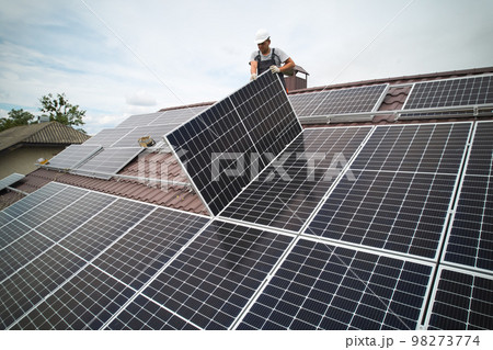 Man technician mounting photovoltaic solar moduls on roof of house. Mounter in helmet installing solar panel system outdoors. Concept of alternative and renewable energy. Aerial view. Man technician mounting photovoltaic solar moduls on roof of house. Mounter in helmet installing solar panel system outdoors. Concept of alternative and renewable energy. Aerial view. 98273774