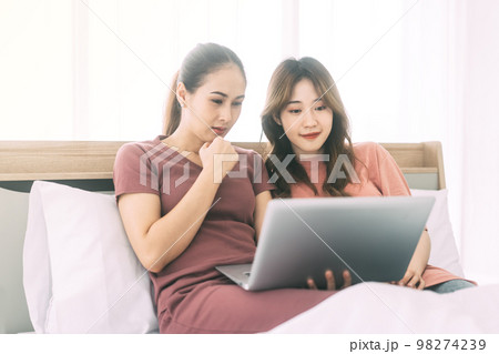 Two young adult woman living together with relationship laying at bedroom talking about work 98274239