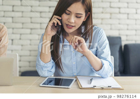 Asian women talk via smartphone work from home small office desk. Young asian Woman hands holding phone technology lifestyle. Happy Women person calling use digital smart phone working home office 98276114