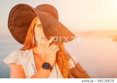 Portrait of happy young woman wearing summer black hat with large brim at beach on sunset. Sensual girl covering half face with hat on beach. Happy young woman smiling and looking at camera at sea. Portrait of happy young woman wearing summer black hat with large brim at beach on sunset. Sensual girl covering half face with hat on beach. Happy young woman smiling and looking at camera at sea. 98276679