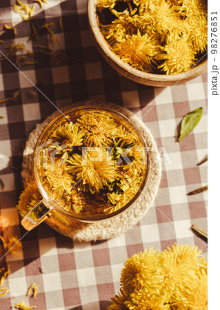 Dandelion flower healthy tea in glass cup on table. Herbal medicine Delicious tisane tea from with fresh yellow blossom dandelion flowers inside tea cup. Green clearing infusion Wildflowers Eco 98276851