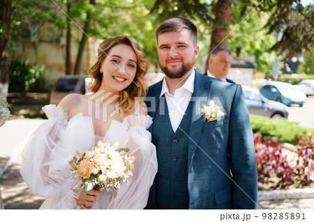 happy groom and bride in dress with open shoulders and a bouquet on the street. 98285891