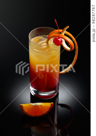 Cocktail tequila sunrise on a black reflective background. Cocktail tequila sunrise on a black reflective background. 98287767