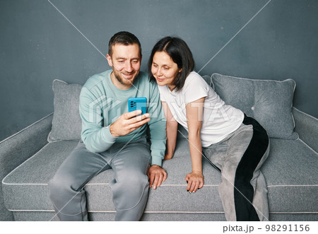 Young couple relaxing on sofa using mobile smart phone relaxing at home Young couple relaxing on sofa using mobile smart phone relaxing at home 98291156