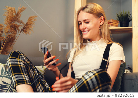 Young woman using mobile phone. Sitting on the couch. Stay home concept during coronavirus covid-2019 Young woman using mobile phone. Sitting on the couch. Stay home concept during coronavirus covid-2019 98292615