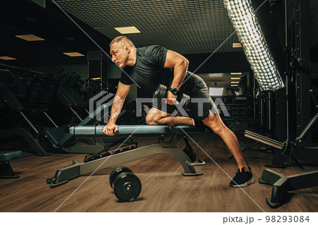 Muscular young man lifting weights in a dark gym Muscular young man lifting weights in a dark gym 98293084