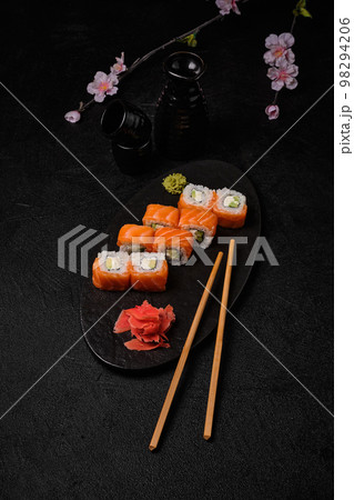 salmon sushi roll with red caviar, chopsticks, bottle of sake and cups on black salmon sushi roll with red caviar, chopsticks, bottle of sake and cups on black 98294206