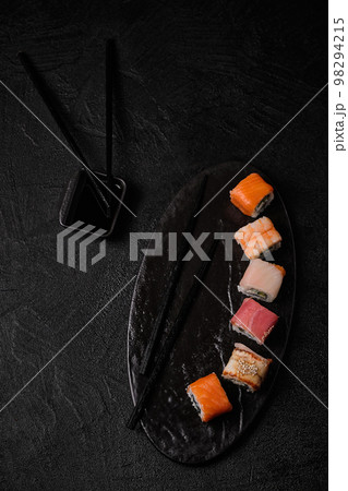Different kind of sushi roll, soy sauce and chopsticks on black concrete background Different kind of sushi roll, soy sauce and chopsticks on black concrete background 98294215