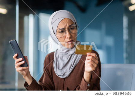 Upset and disappointed woman in hijab inside office trying to make purchase in online store, business woman holding smartphone and bank credit card, received money transfer error. Upset and disappointed woman in hijab inside office trying to make purchase in online store, business woman holding smartphone and bank credit card, received money transfer error. 98294636