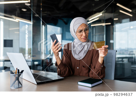 Upset and disappointed woman in hijab inside office trying to make purchase in online store, business woman holding smartphone and bank credit card, received money transfer error. Upset and disappointed woman in hijab inside office trying to make purchase in online store, business woman holding smartphone and bank credit card, received money transfer error. 98294637