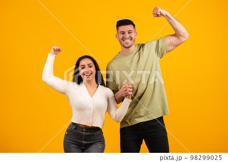 Smiling millennial arabic husband and wife holding hands, show biceps on hand Smiling millennial arabic husband and wife holding hands, show biceps on hand 98299025
