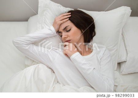 Top view of unhappy woman lying in bed, touching head Top view of unhappy woman lying in bed, touching head 98299033