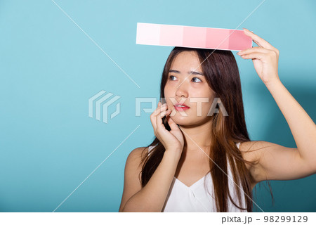 Asian beautiful young woman holding skin color scale paper studio shot isolated on blue background, Portrait of happy female hold color card under sun protection, skin beauty face 98299129