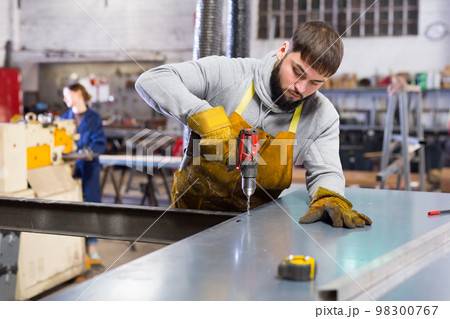 Man engineer drilling metal sheet in workshop 98300767