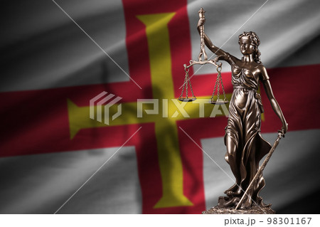 Guernsey flag with statue of lady justice and judicial scales in dark room. Concept of judgement and punishment 98301167