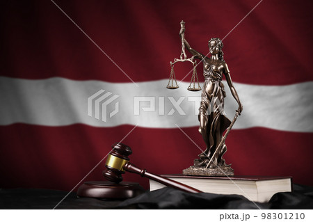 Latvia flag with statue of lady justice, constitution and judge hammer on black drapery. Concept of judgement and guilt 98301210
