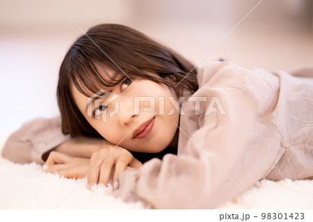 カーペットに寝転んでくつろぐ若い女性 98301423