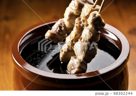 鶏のモモ肉の串焼きをタレ壺の中の焼き鳥のタレに漬ける 98302244