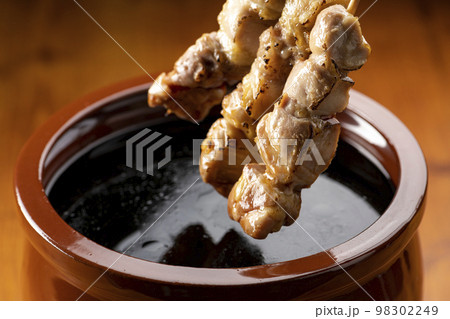 鶏のモモ肉の串焼きをタレ壺の中の焼き鳥のタレに漬ける 鶏のモモ肉の串焼きをタレ壺の中の焼き鳥のタレに漬ける 98302249