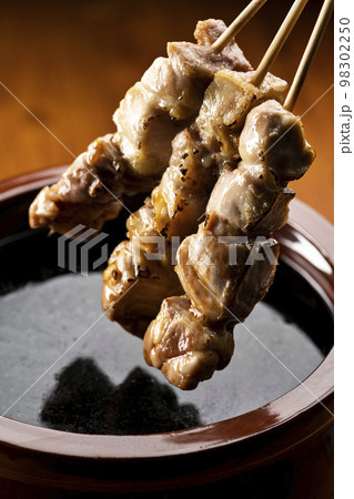 鶏のモモ肉の串焼きをタレ壺の中の焼き鳥のタレに漬ける 98302250