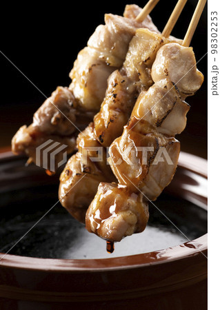 鶏のモモ肉の串焼きをタレ壺の中の焼き鳥のタレに漬ける 98302253
