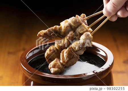 鶏のモモ肉の串焼きをタレ壺の中の焼き鳥のタレに漬ける 鶏のモモ肉の串焼きをタレ壺の中の焼き鳥のタレに漬ける 98302255