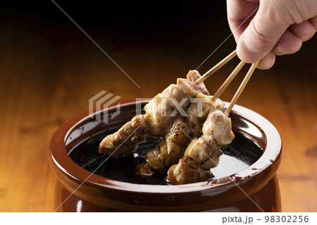 鶏のモモ肉の串焼きをタレ壺の中の焼き鳥のタレに漬ける 鶏のモモ肉の串焼きをタレ壺の中の焼き鳥のタレに漬ける 98302256