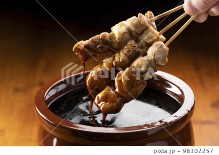 鶏のモモ肉の串焼きをタレ壺の中の焼き鳥のタレに漬ける 98302257