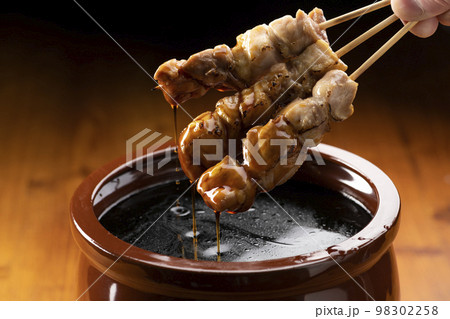 鶏のモモ肉の串焼きをタレ壺の中の焼き鳥のタレに漬ける 98302258
