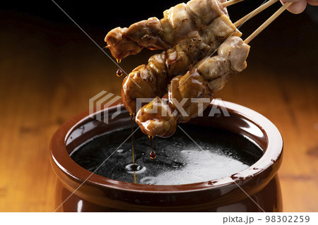 鶏のモモ肉の串焼きをタレ壺の中の焼き鳥のタレに漬ける 98302259