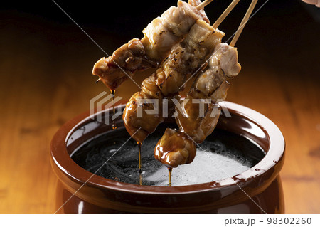 鶏のモモ肉の串焼きをタレ壺の中の焼き鳥のタレに漬ける 鶏のモモ肉の串焼きをタレ壺の中の焼き鳥のタレに漬ける 98302260