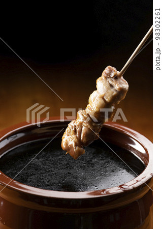 鶏のモモ肉の串焼きをタレ壺の中の焼き鳥のタレに漬ける 98302261